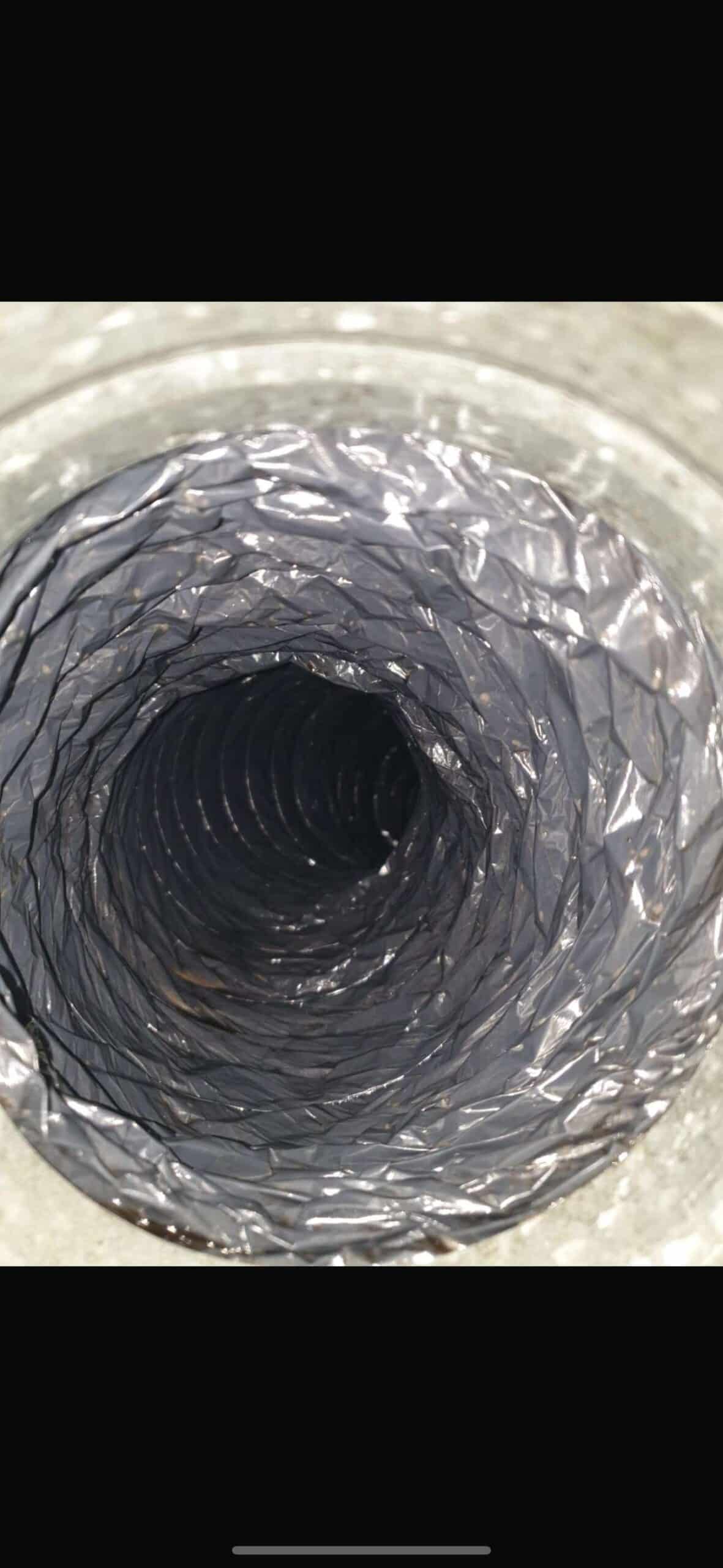 A close-up view of the interior of a metallic, spiral duct or tunnel, showing concentric circular layers with a shiny, textured surface. The image creates a sense of depth and symmetry.