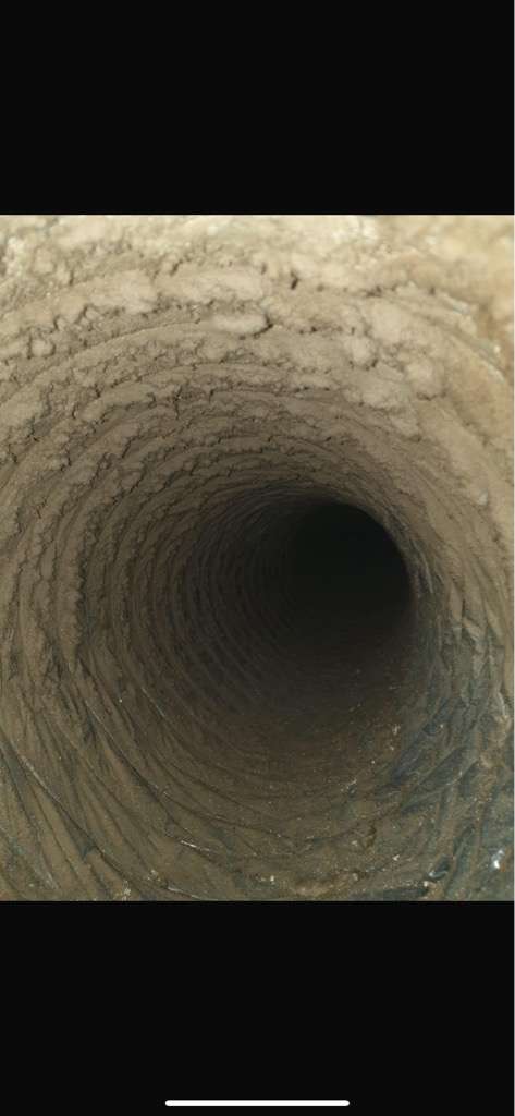 A close-up view of a deep, cylindrical hole or tunnel with ribbed, earthy walls, stretching into the darkness.