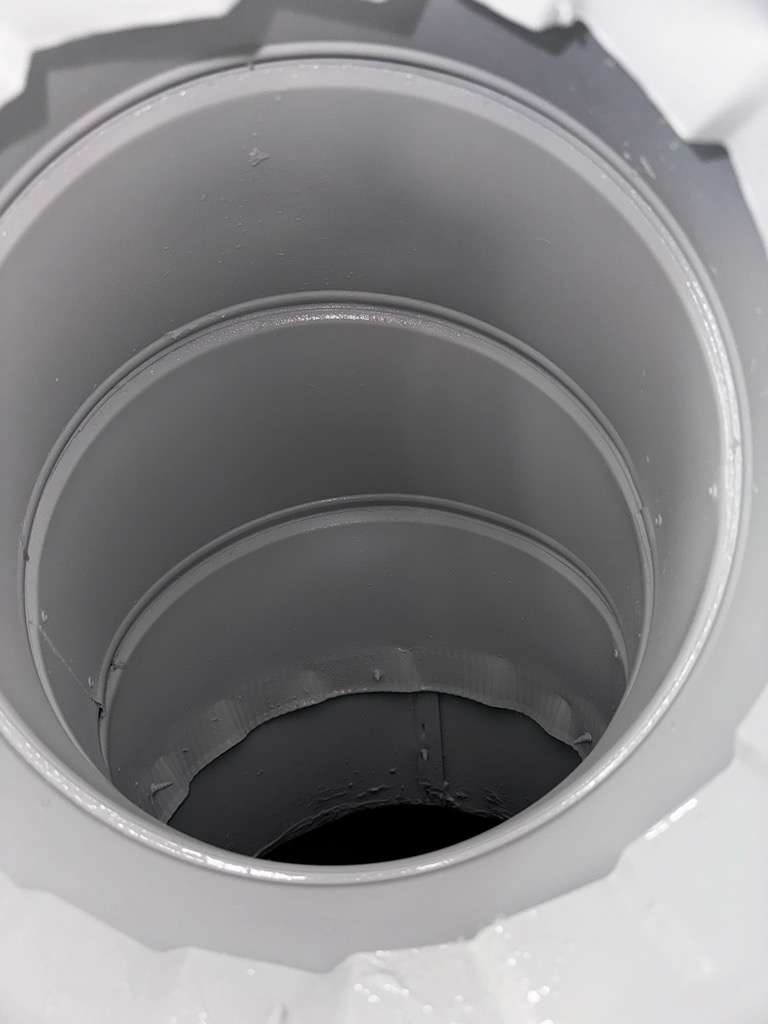 Close-up of the interior of a large, empty, cylindrical metal container or pipe with a smooth, shiny surface. The perspective captures concentric rings leading toward the dark center, creating a tunnel-like effect.